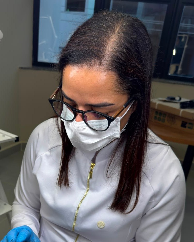 Isa de Paula, de jaleco e óculos, atendendo uma paciente na clínica